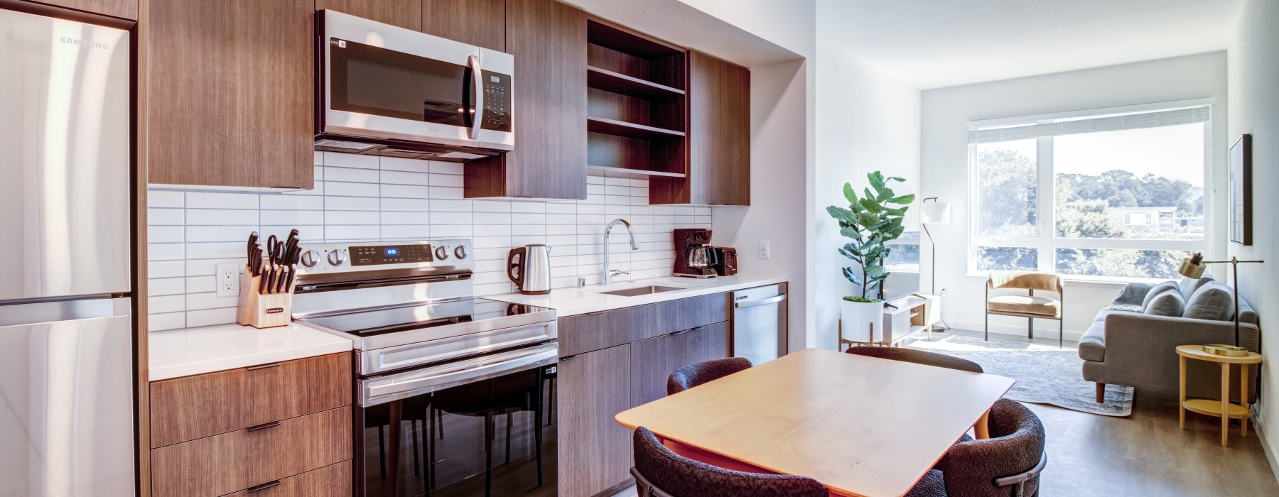 Large apartment with a kitchen with darker wood cabinets, white tile backsplash and a living room in the distance.