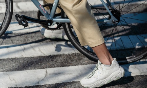 photo of a mans legs while riding a blue bicycle he has white shoes and his ankle is showing.