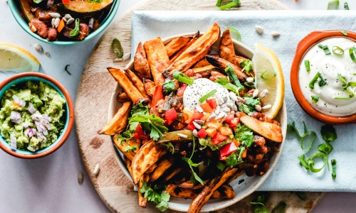 Three bowls of food on a table one with guacamole, one with fries and seasoning and one with ranch.