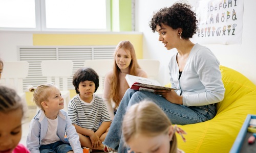 eacher reading a book to a group of young children during story time in a classroom.
